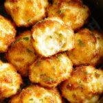 Golden crispy cheesy mashed potato puffs freshly cooked in an air fryer, showcasing their light, airy interior and cheesy exterior.