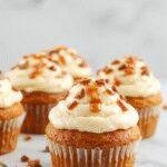 Freshly baked pumpkin cupcakes topped with salted caramel cream cheese frosting, garnished with a sprinkle of cinnamon and caramel drizzle.